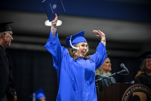 Photo of a graduate celebrating as they walk across the stage.