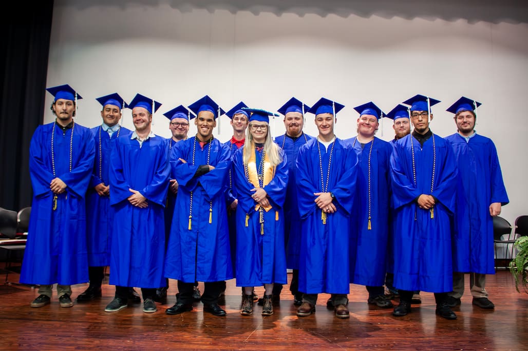 Photo of a group of graduates wearing their caps and gowns and standing on a stage.