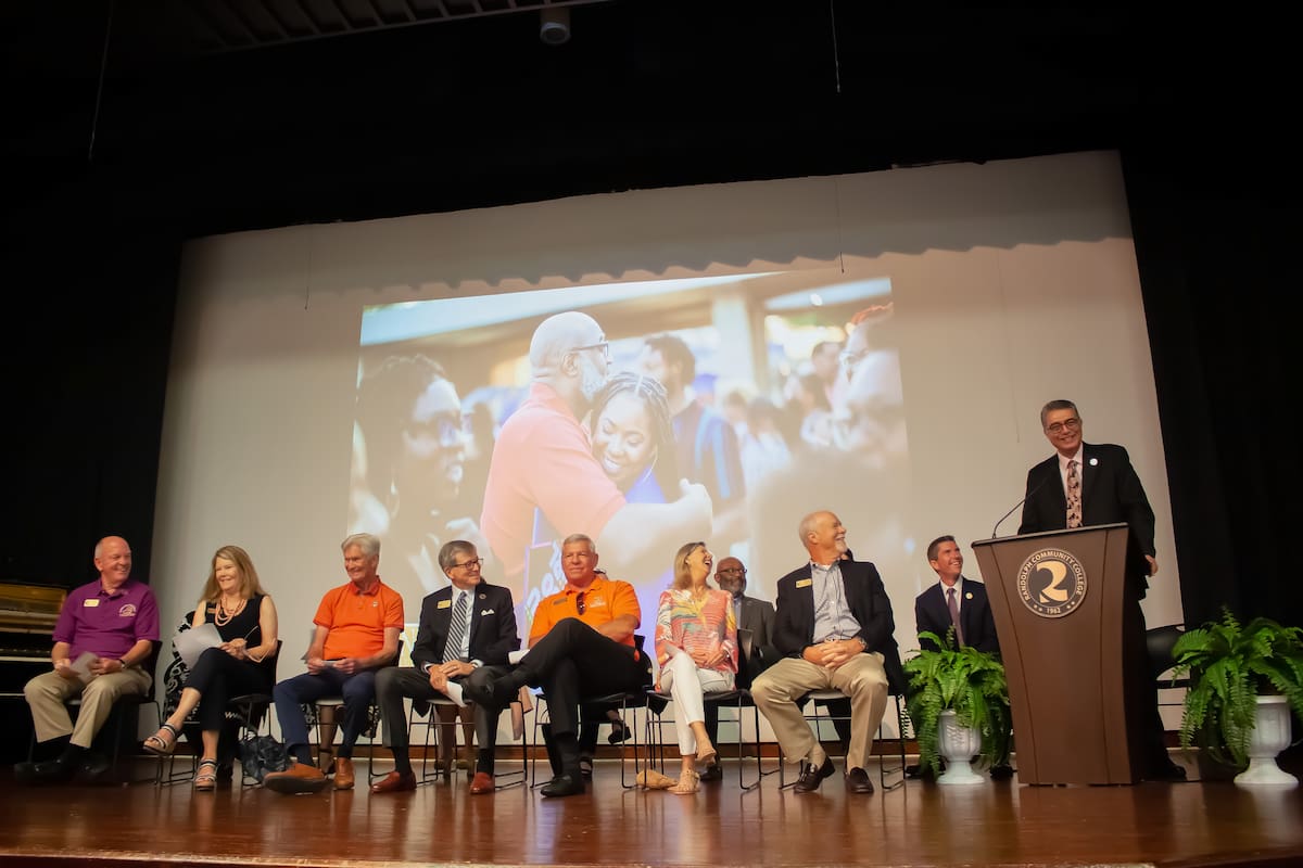 Photo of a person speaking at a podium on a stage, while people on the stage are sitting.