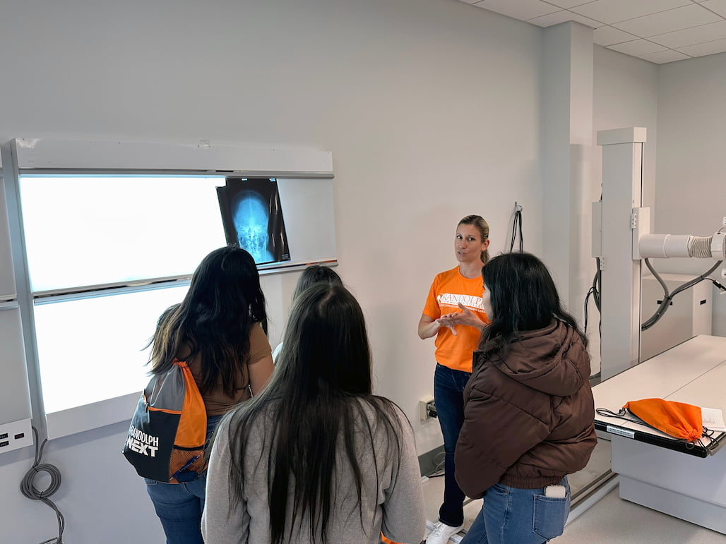 Photo of a woman standing in front of an x-ray of a skull and speaking to students.