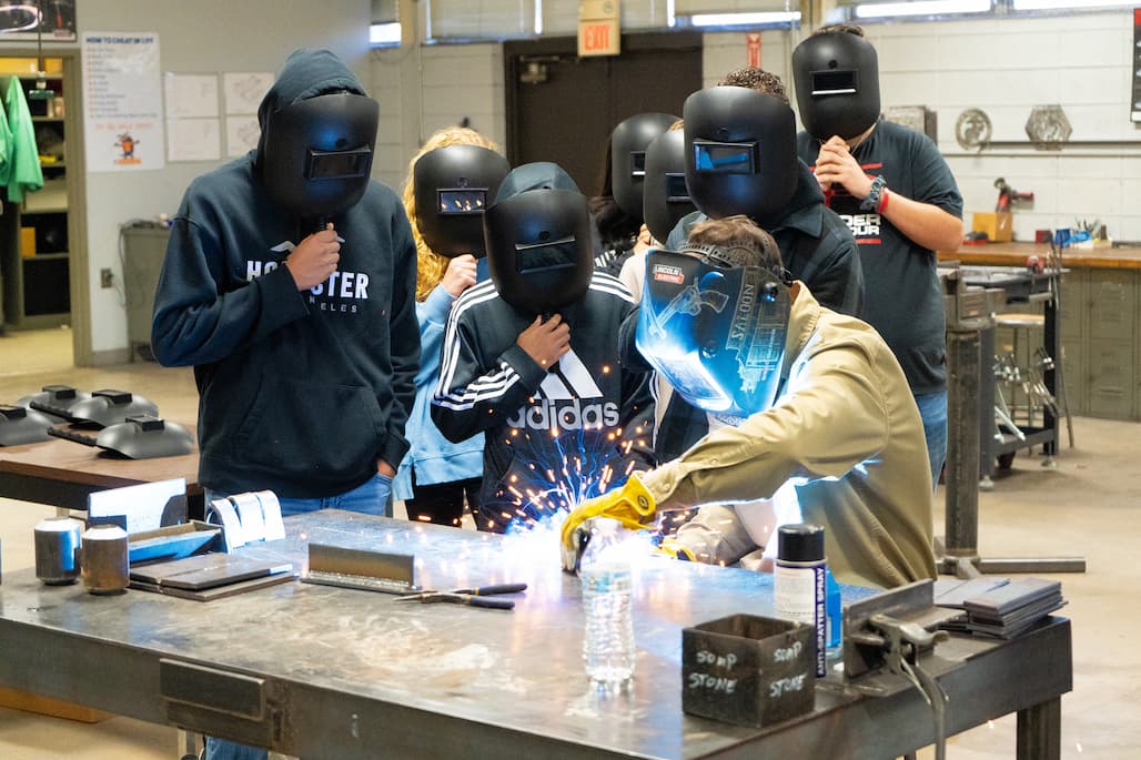 Photo of a person welding while a group of people watches.