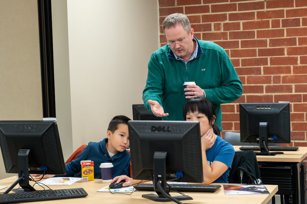 Photo of a person helping someone filling out a form on a computer.