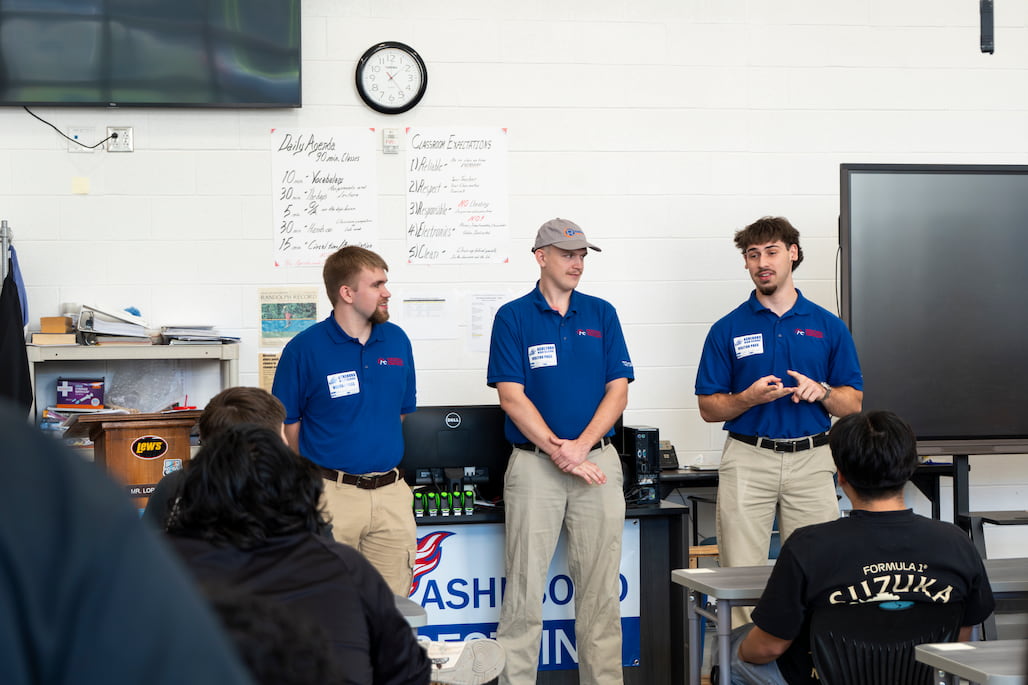 Photo of three people speaking in front of a classroom.