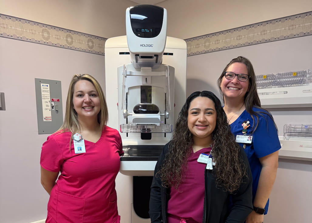 Photo of three people standing in front of a mammography machine.