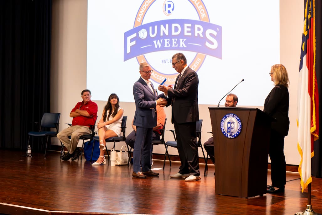 Photo of a man giving another man an award on a stage.
