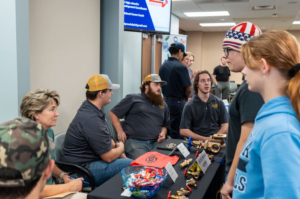 Photo of a group of people sitting at a table and talking to students in the JB and Claire Davis Corporate Training Center at Randolph Community College.
