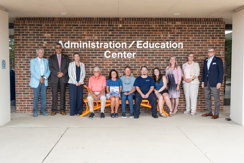 Group photo of RCC administrators and Wanda Brown's family sitting on the bench dedicated to longtime employee Wanda Brown in front of the Administration/Education Center.