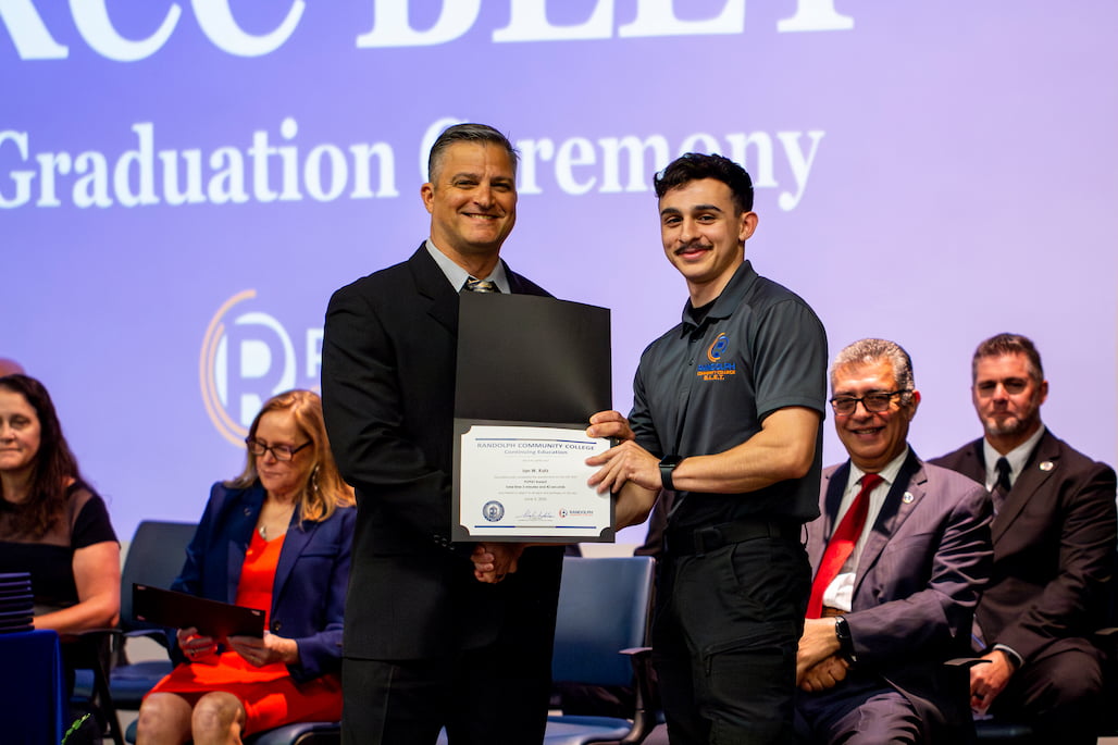 Photo of two people shaking hands and holding an award.