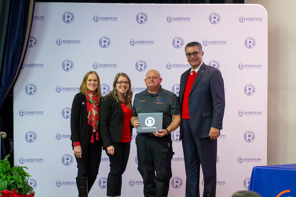 Photo of a group of people standing in front of a backdrop with RCC logos on it.