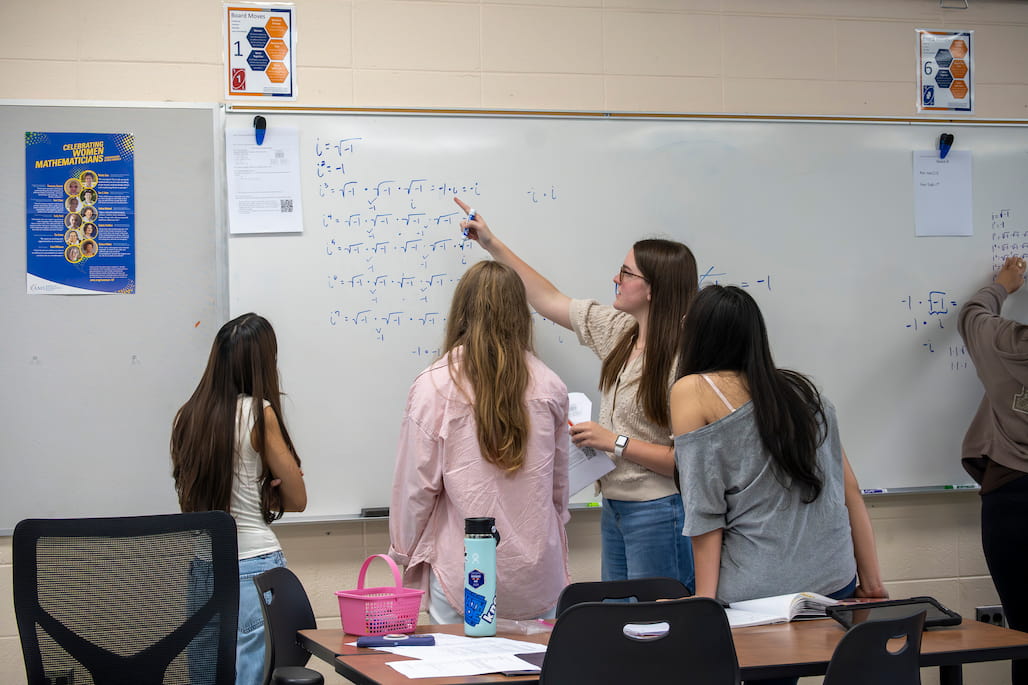 A group of students solves a math problem on a whiteboard.