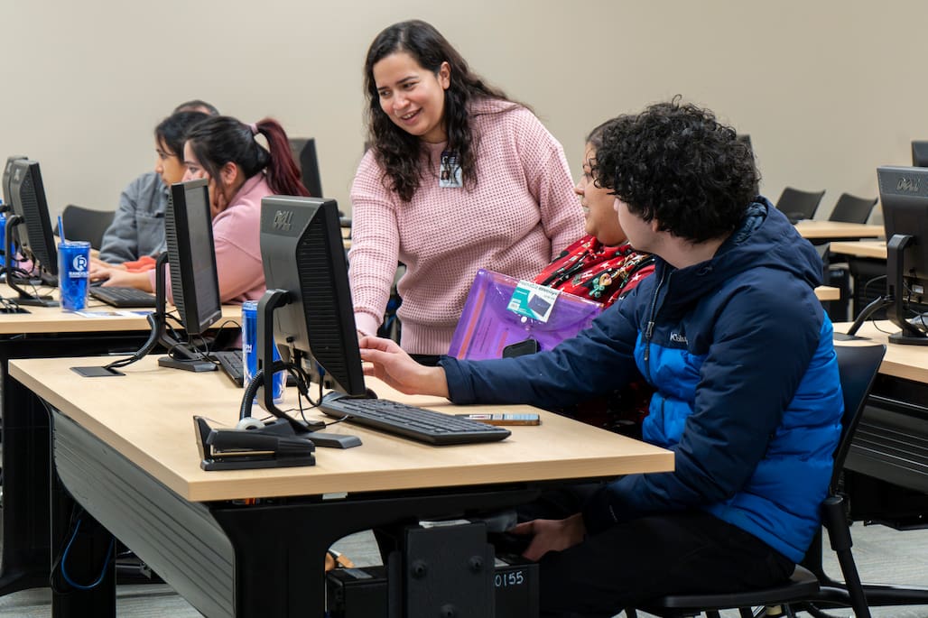 Photo of a person helping another person on the computer.